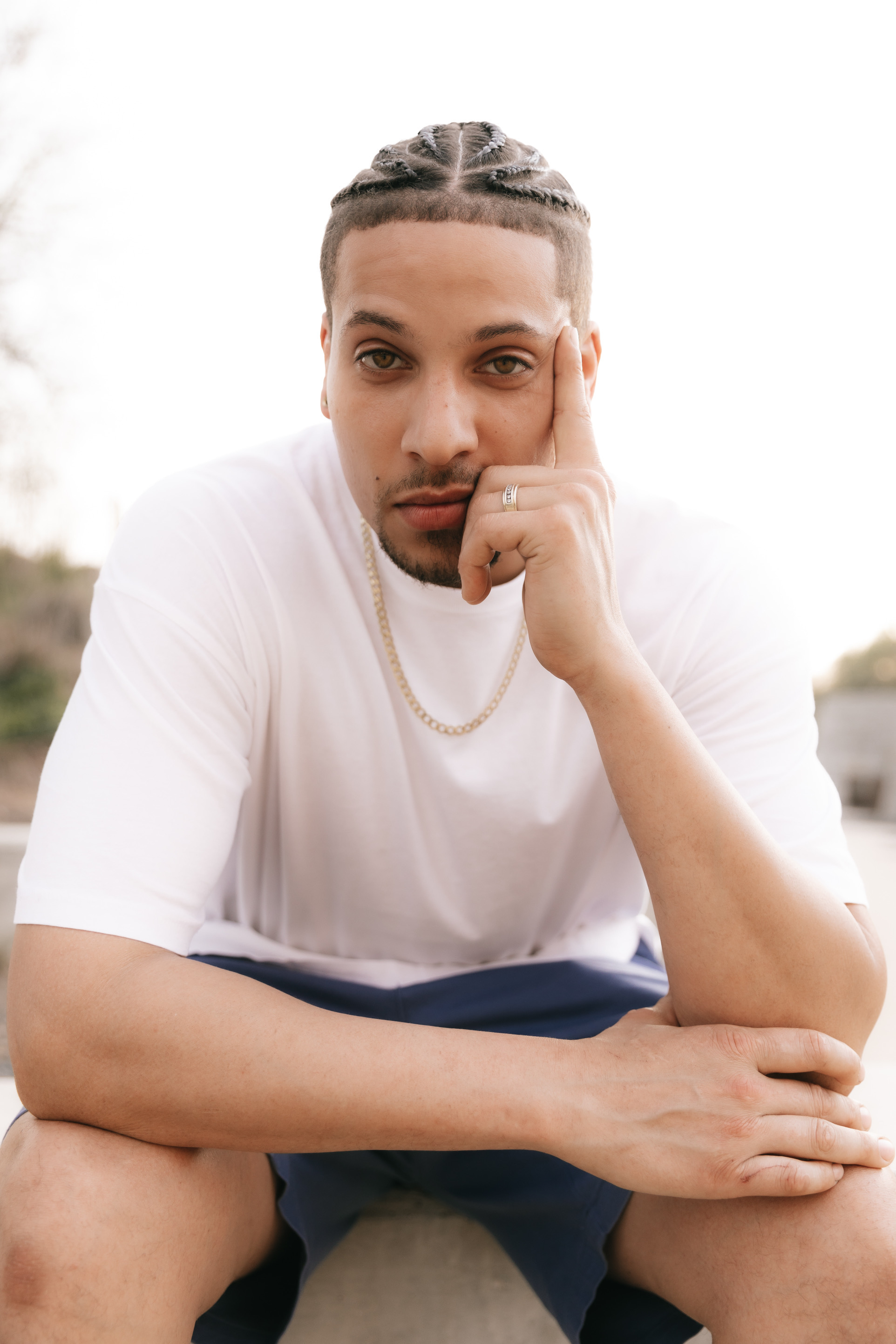 B_RocKing10 in a white tee and gold chain, seated outdoors