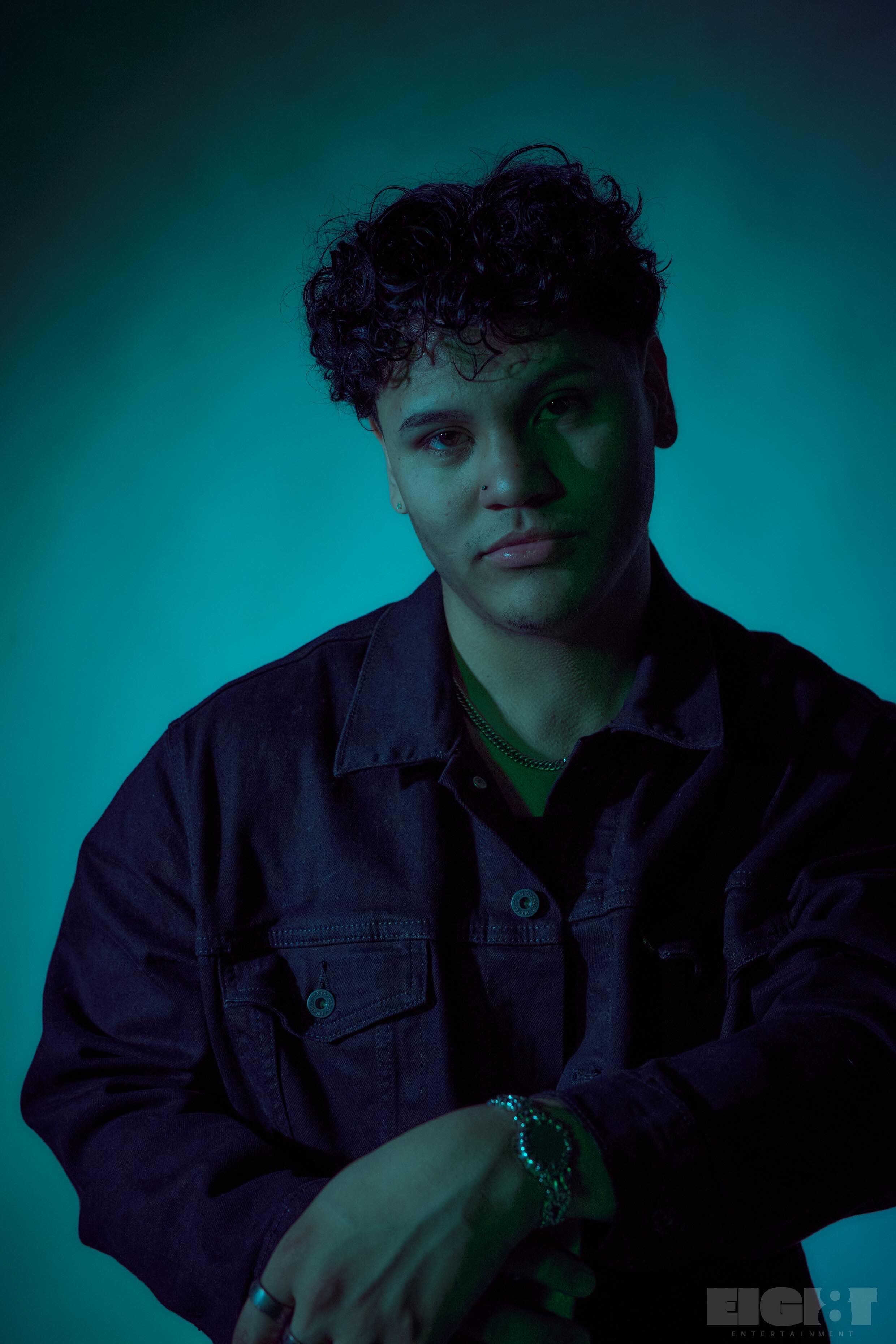 Evver the Thinker, an Austin artist, in a teal-lit studio portrait wearing a dark denim jacket