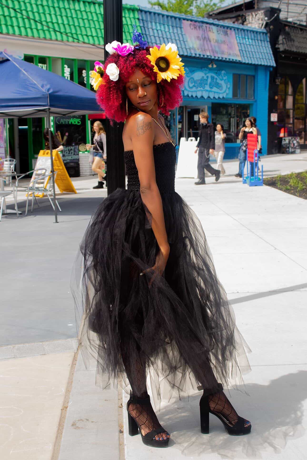 Ife Devine in a black tulle dress with sunflowers and roses in her hair, on an urban street