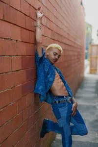 KaliiFreak posing against a red brick wall in a patterned denim outfit