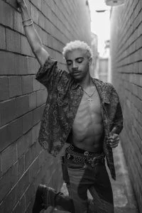 KaliiFreak in a black-and-white portrait leaning against a brick alley wall