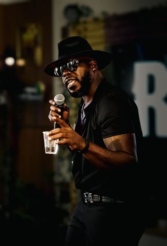Teknition at RRL 2026, in black fedora and sunglasses singing into the mic while holding a cup