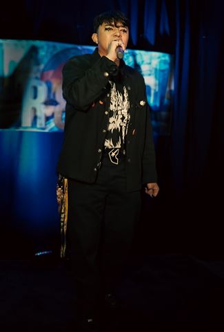 Untitled Flows at RRL 2026, in black jacket and star eye makeup singing into the mic before the blue-lit backdrop