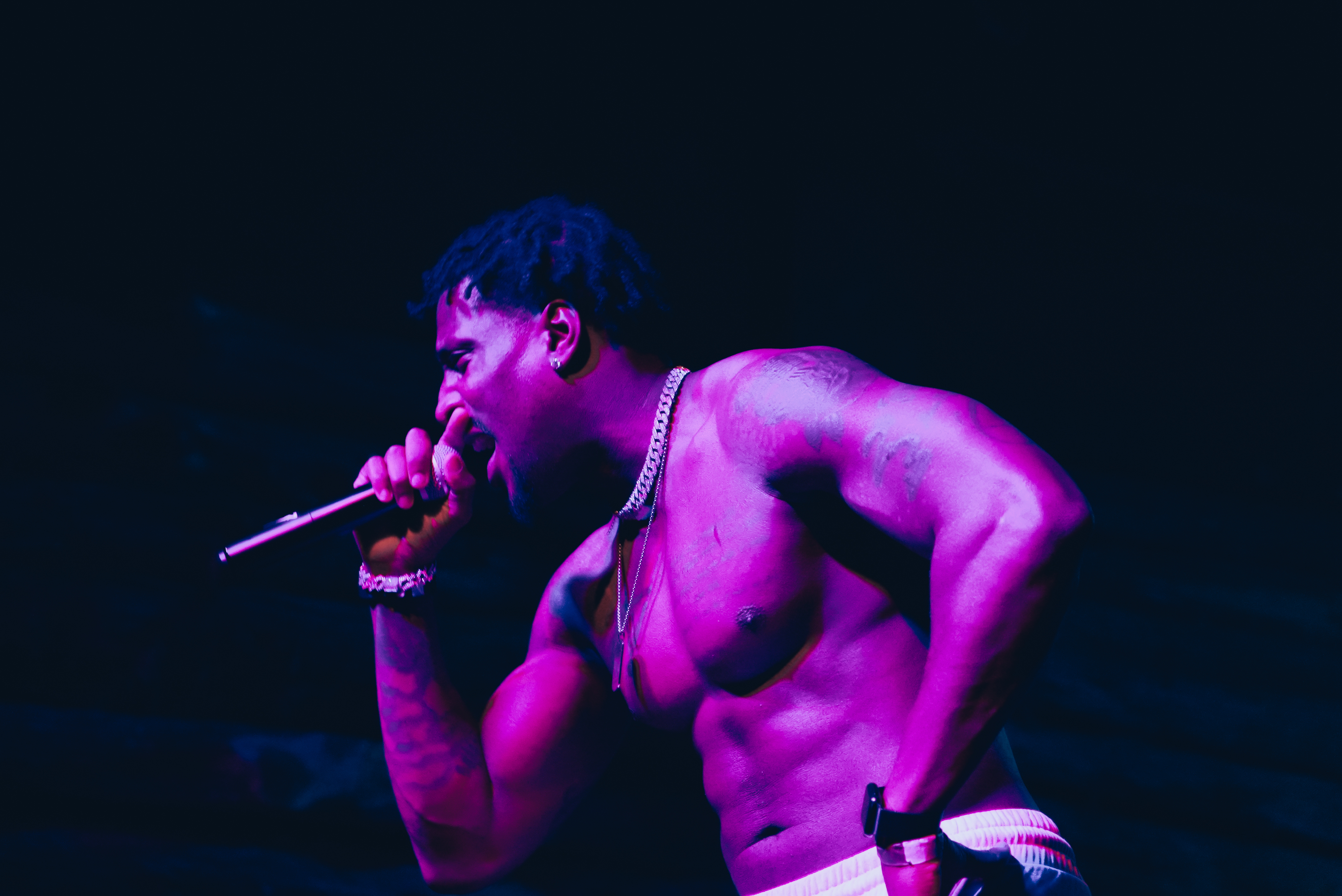 Tay No Tee on stage in dramatic purple and red light, mic in hand